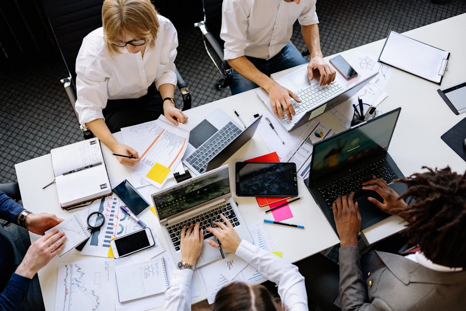 Vibrant office teamwork scene with laptops, documents, and diverse professionals in a meeting.